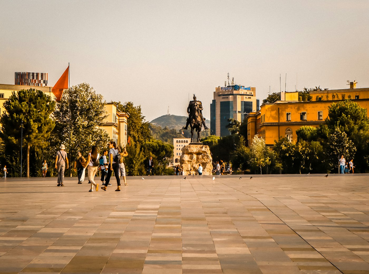 Skanderbeg Square in Tirana at golden hour, with the Skanderbeg equestrian statue, the Albanian flag and the ochre ministry buildings
